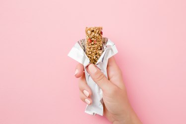 woman's hand holding cereal bar on pastel pink background