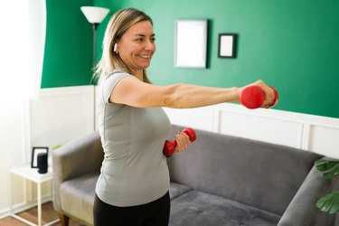 older woman doing the IYT raise exercise with a pair of dumbbells in her living room.