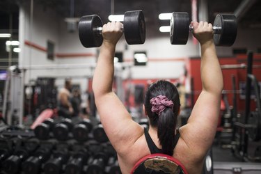 Rear view of strong woman exercising with dumbbells  at the gym.
