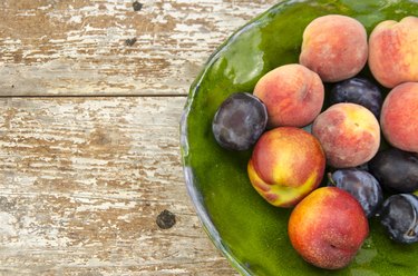 whole peaches and plums in bowl on wooden background