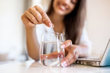 Closeup of a young woman dropping an effervescent antacid in a glass of water. young woman hardly put a soluble pill with a medicine for pain or a hangover in a glass of water