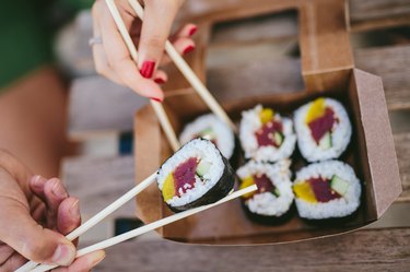 friends hands eating gluten-free sushi from takeout box