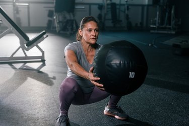 Woman doing a squat variation with a black medicine ball