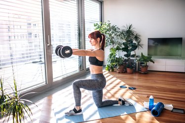 woman doing a dumbbell strength training workout on a blue yoga mat at home
