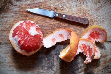overhead photo of a paring knife next to a partly peeled red grapefruit