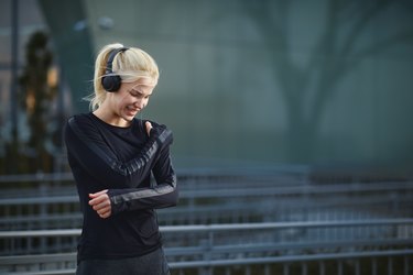 女人穿着黑色健身器材和耳机手里拿着她的肩膀疼痛而外