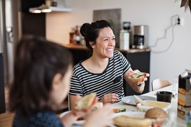 Smiling person with brown hair in a bun eating breakfast at home with her family, to represent a morning habit for balanced blood sugar