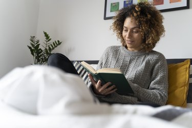 Woman sitting on bed, reading book