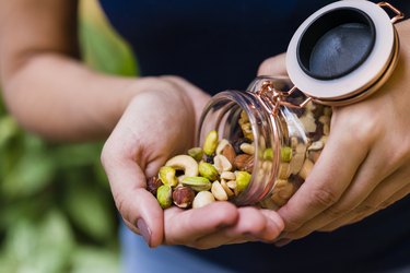 a close up of a person pouring a glass jar of mixed nuts into one hand