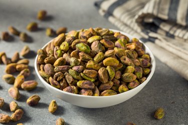 Raw Organic Salted and Roasted Pistachios with health benefits for your heart, brain, gut and more in a white bowl.