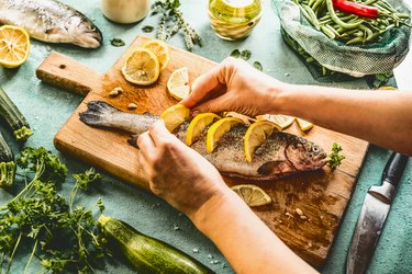 an overhead photo of a person preparing a whole fish with lemon on a wooden cutting board