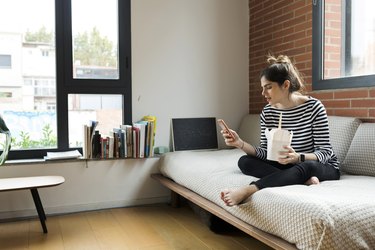 年轻女子坐在家里的沙发上吃着外卖