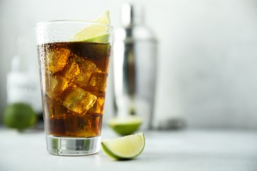 a glass of diet cola with ice and slices of lime on a white counter