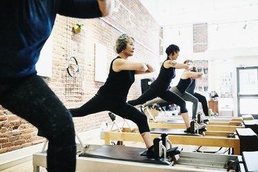 Mature group balancing on reformers while doing roman splits during class in pilates studio