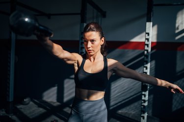 strong young caucasian woman doing a single-arm kettlebell swing as one of the best compound exercises for abs