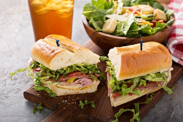 Subway sandwich with Subway Sweet Onion Sauce on a cutting board with salad and beverage.