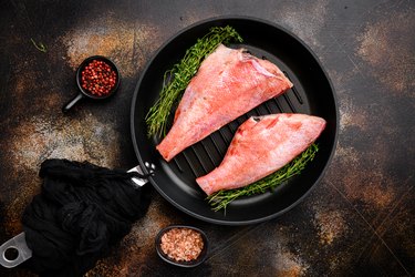 Red sea perch raw whole fresh fish, in frying cast iron pan, on old dark rustic table background, top view flat lay, with copy space for text