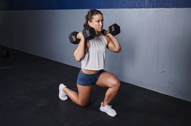 Person in shorts and a crop top with a ponytail does a dumbbell lunge to build muscle and tighten skin