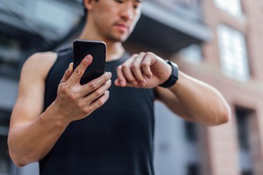 close up of a person in a black tank top using half-marathon training app on smart phone and a running watch on their wrist