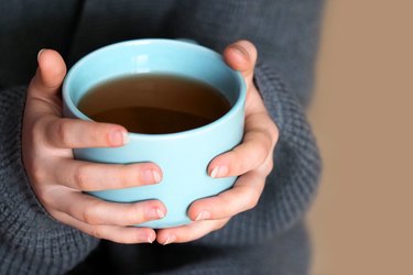 Female hands holding a big cup of coffee, home comfort. Girl in oversize knitted sweater