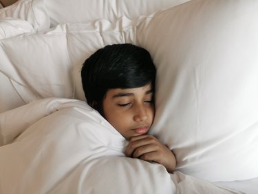8-year-old boy sleeping in a white bed after taking a melatonin dose based on a weight melatonin dosage chart by age