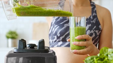 Sporty woman making healthy green fresh smoothie by blender for healthy drink, including vegetable and fruits