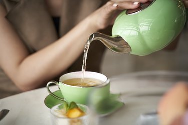 close-up of woman pouring hot tea from kettle