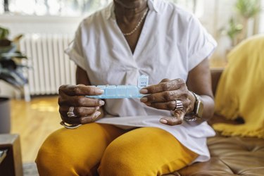 close view of a person in yellow pants and white shirt sitting on a couch and taking pills from a pill organizer