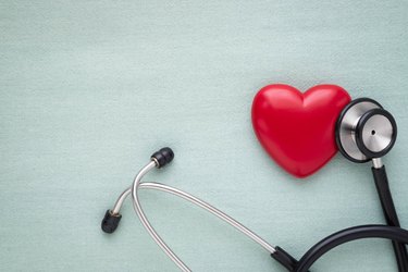 Black stethoscope with red heart of doctor for check up on light green background. Stethoscope equipment of medical use to diagnose hear sound. Health care and cardiology concept with copy.