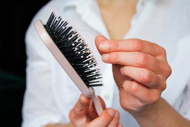 Close-up photo of a person picking hair out of a pink hairbrush, due to hair loss.
