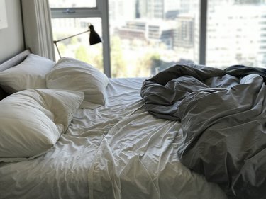 an empty, unmade bed with wrinkled sheets in front of a sunny window