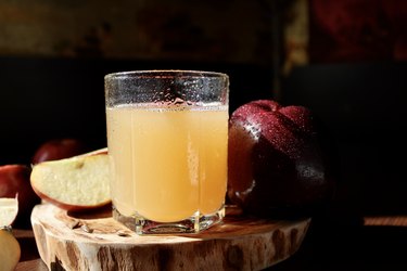 Glass of apple cider and red apples on a wooden stand on a dark background