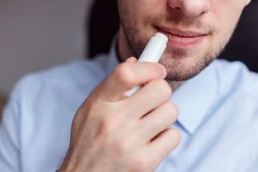 Man applying hygienic lip balm on lips to revive chapped lips and avoid dry, closeup