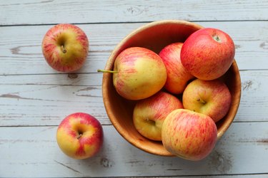 top view of a bunch of red apples in a wooden bowl on a wooden table