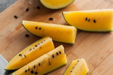 L-citrulline-rich sliced yellow watermelon with seeds on a cutting board.