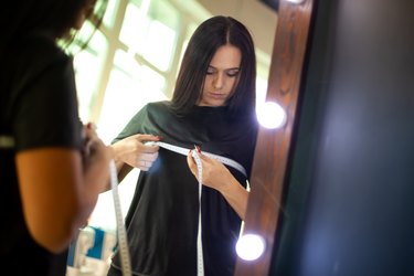 designer measuring breast size after losing weight with tape measure on front of mirror at workshop