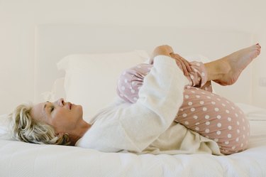 Mature person with blond hair doing the knees to chest stretch in bed for morning back pain