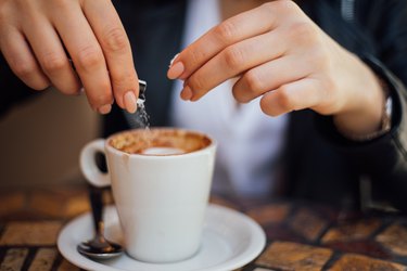 woman's hands pouring aspartame sugar packet into coffee