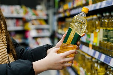 Woman choosing oil in the supermarket. Close up of hand holding bottle of oil at store.