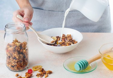 Close up of woman pouring milk into bowl with granola