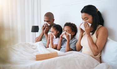 a family of four people in bed together, all blowing their noses because they're sick with the flu