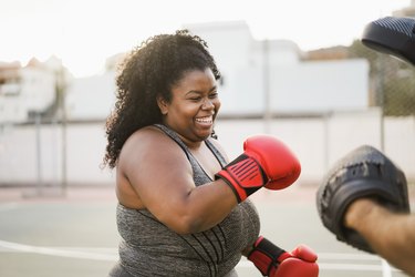 plus-sized black woman doing a boxing workout outside and smiling