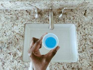 a hand holding a cup of blue mouthwash over a bathroom sink