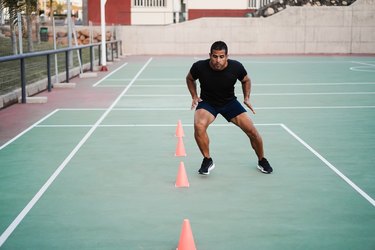 Hispanic man doing speed and agility cone drills workout session outdoors - Focus on man face