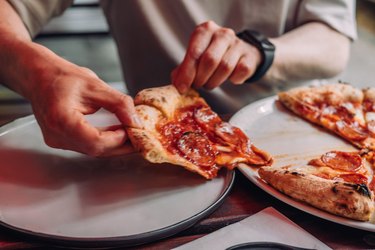 Hands grabbing a slice of pepperoni pizza off the tray