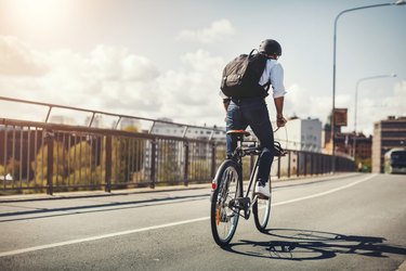 Rear view of man wearing backpack and helmet riding best bike for adults on bridge in city