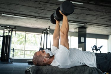 fit man bench pressing dumbbells at the gym during covid-19 pandemic