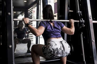 Woman does Smith machine squats at the gym or fitness club.