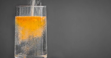Powdered orange fiber supplement for constipation being poured into a clear glass of water