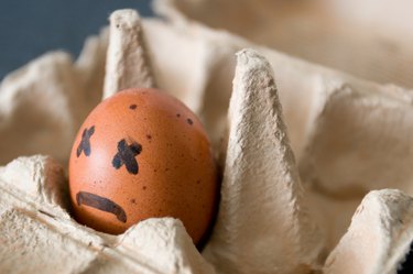 An egg in a carton with a sad face drawn on it, to represent when burps smell like rotten eggs